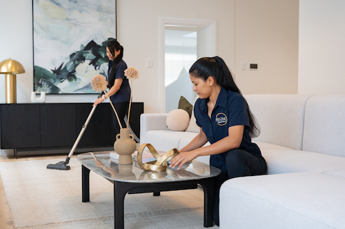 Pristine Housekeepers vacuuming and setting something on the table in a large house.